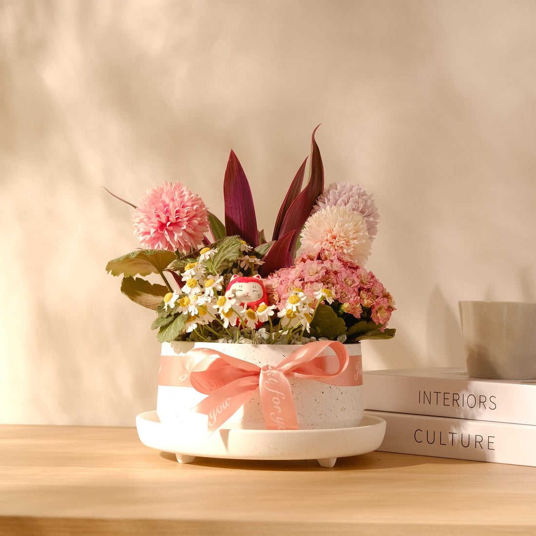 幸福小花園粉色植栽盆景，搭配招財貓與粉色緞帶，放置於有陽光的木桌上